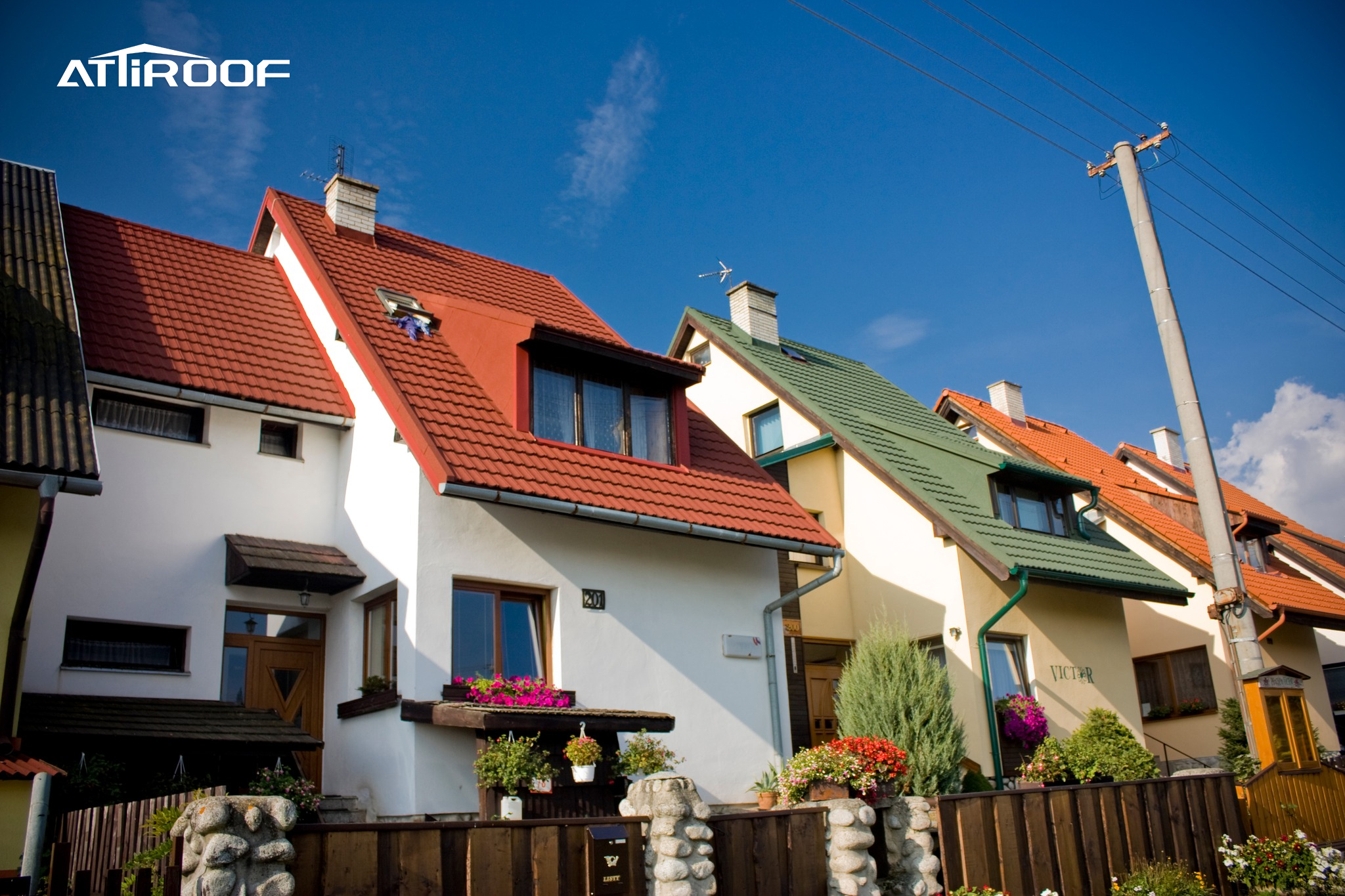 A row of charming houses showcasing a variety of stone-coated metal roof tiles, with a spectrum of red, green, and terracotta colors gleaming under a clear blue sky, complementing the architectural design and adding curb appeal to the neighborhood.