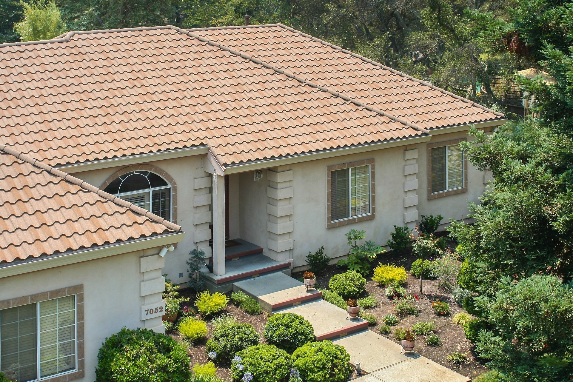 Single-story suburban home with terracotta stone-coated metal roof tiles and landscaped front garden.