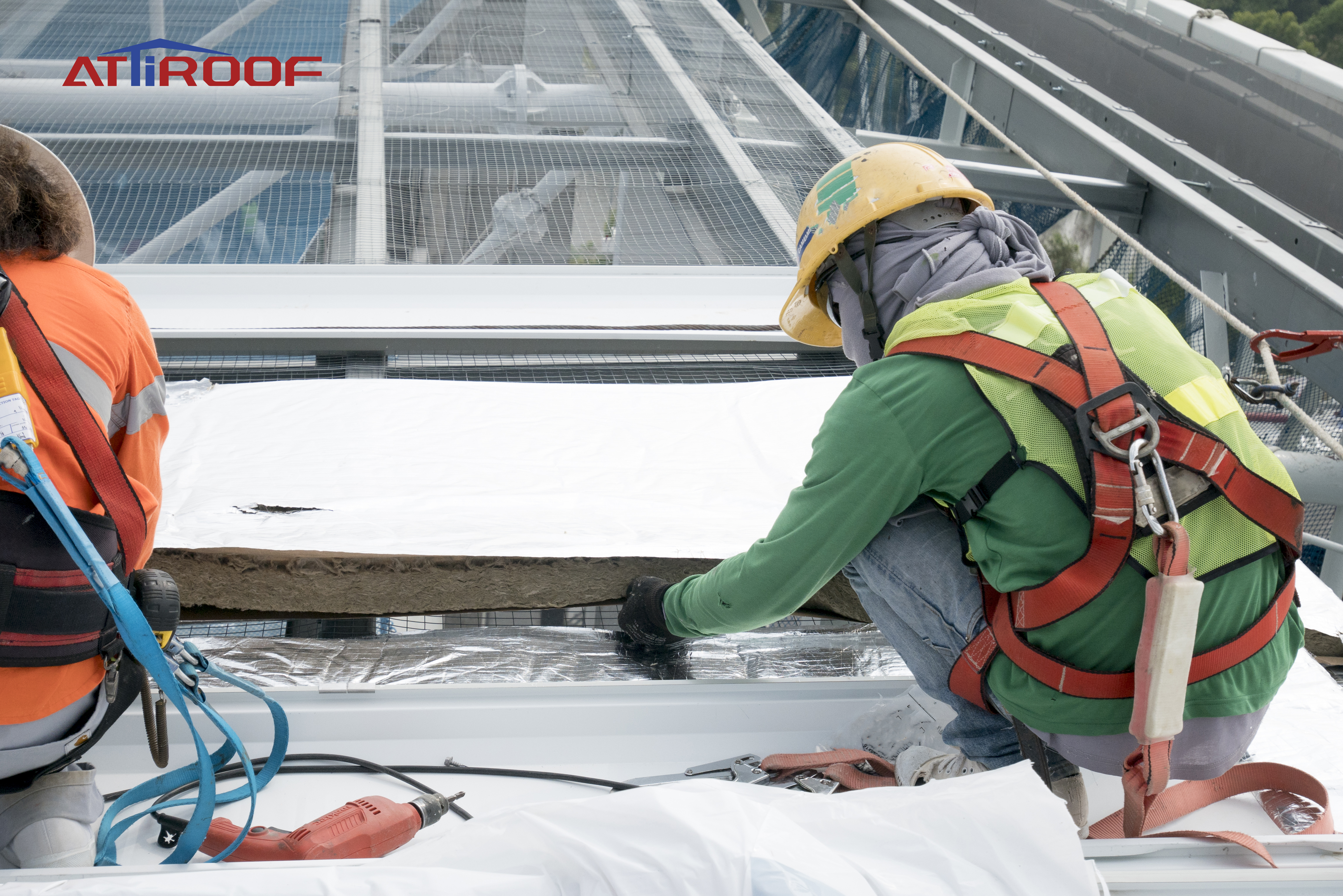 Roof workers with safety harnesses installing roofing materials, demonstrating safety precautions on a rooftop construction site.