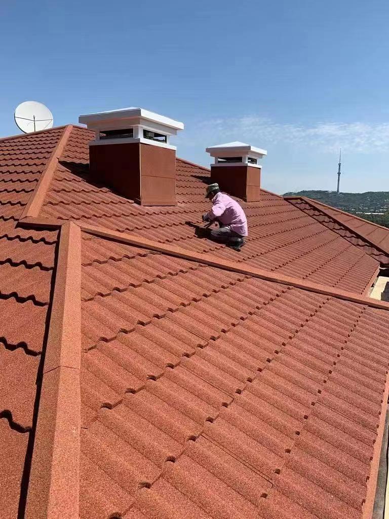 A hardworking worker is engrossed in the installation of stone-coated metal roof tiles on the roof.