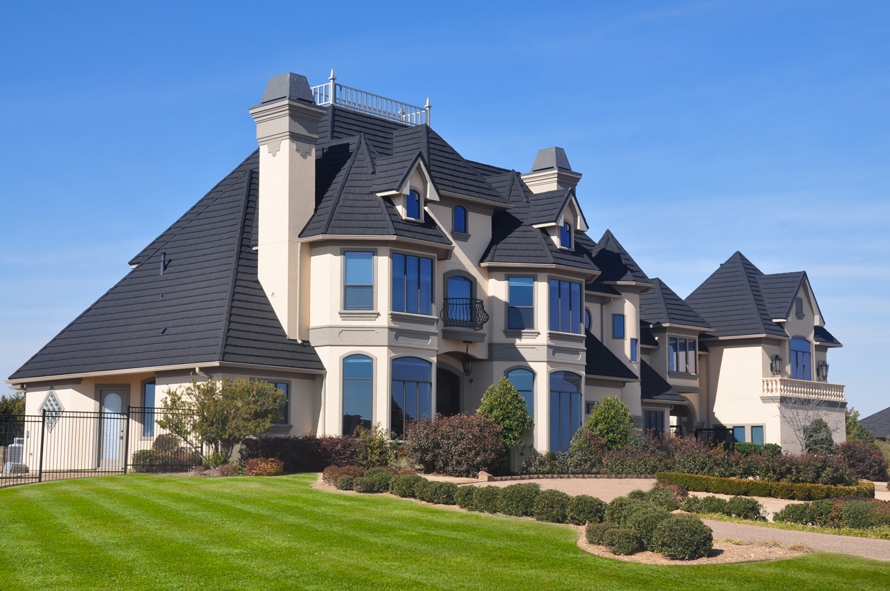 A two-story gray white house with a roof covered with dark colored stone tiles.