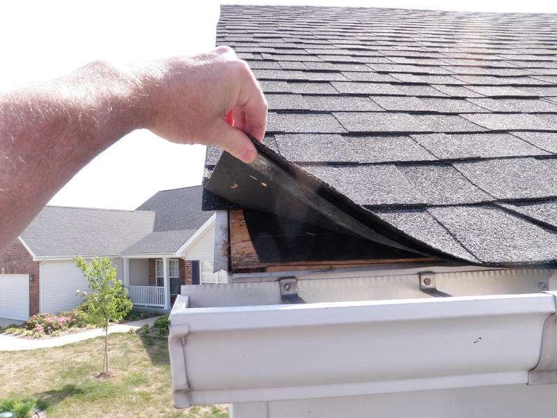 Inspecting a stone-coated metal roof tile for damage near the gutter, highlighting the importance of regular roof maintenance.