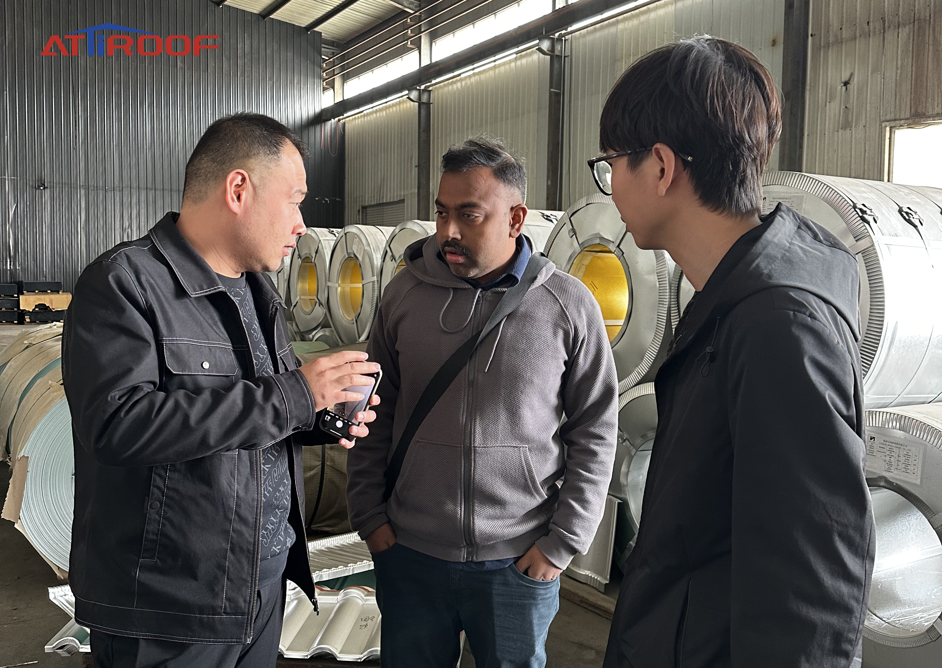 Discussion with suppliers about stone-coated metal roof tile materials in a manufacturing facility.