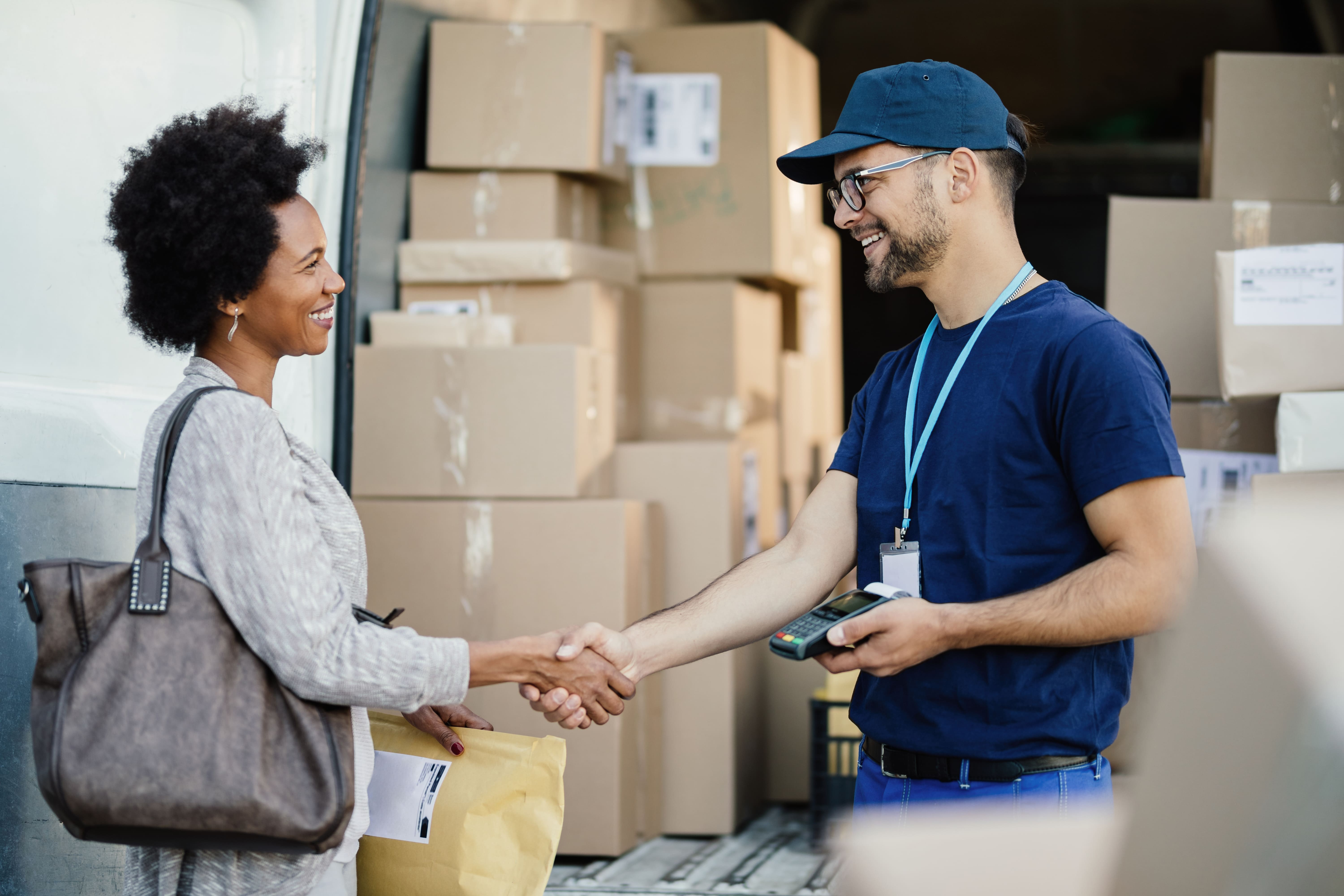 A supplier happily shakes hands with a customer in front of a shipment.